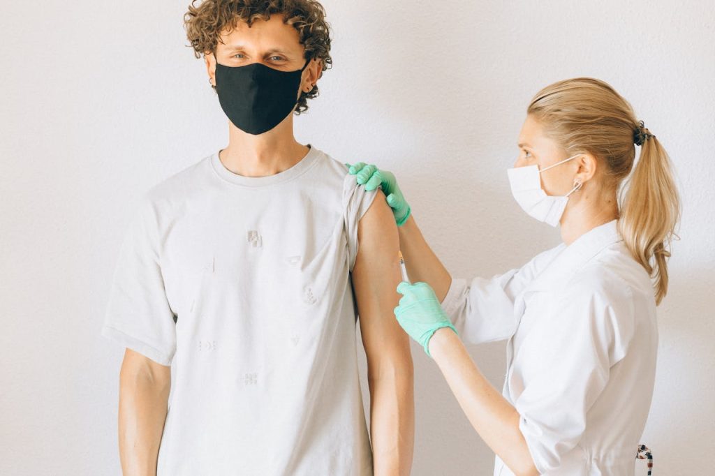 A healthcare worker giving a vaccine injection to a masked man in a clinic.
